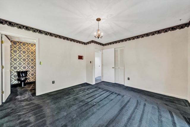 spare room with dark colored carpet, a notable chandelier, and baseboards