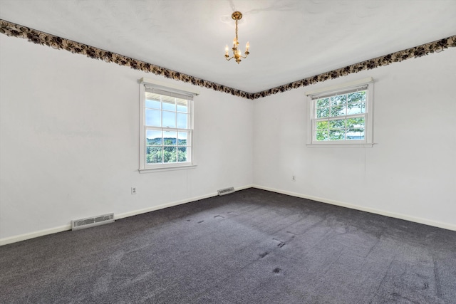 unfurnished room featuring a healthy amount of sunlight, visible vents, dark carpet, and a chandelier