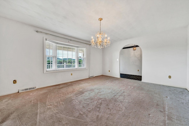 carpeted spare room with visible vents, arched walkways, and a chandelier