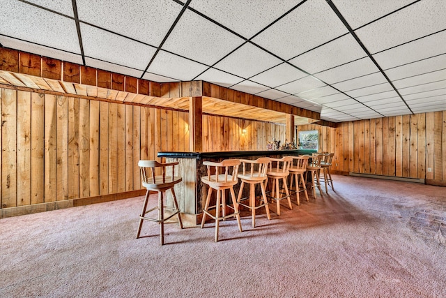 bar with carpet, a dry bar, a baseboard heating unit, wood walls, and a drop ceiling