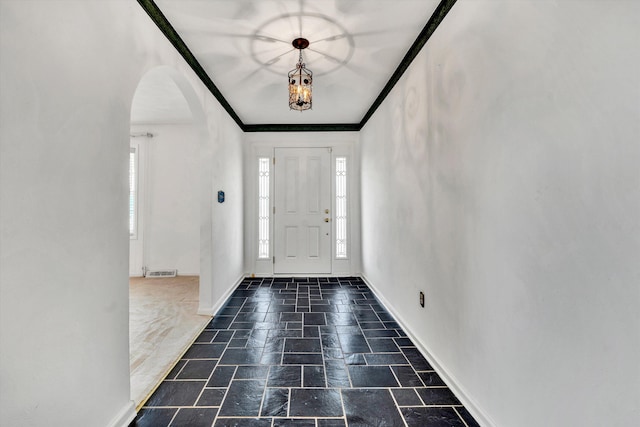 entryway featuring arched walkways, visible vents, baseboards, ornamental molding, and stone tile flooring