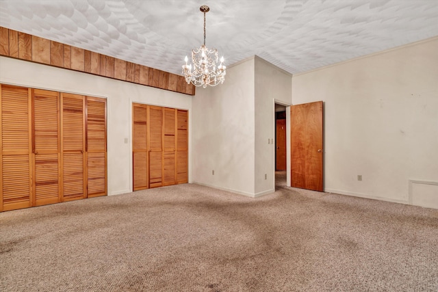 unfurnished bedroom featuring an inviting chandelier, carpet flooring, a textured ceiling, and two closets