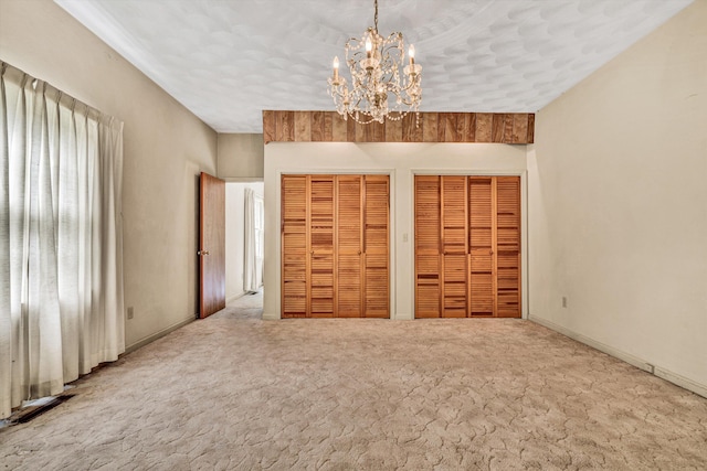 unfurnished bedroom featuring carpet, two closets, and an inviting chandelier