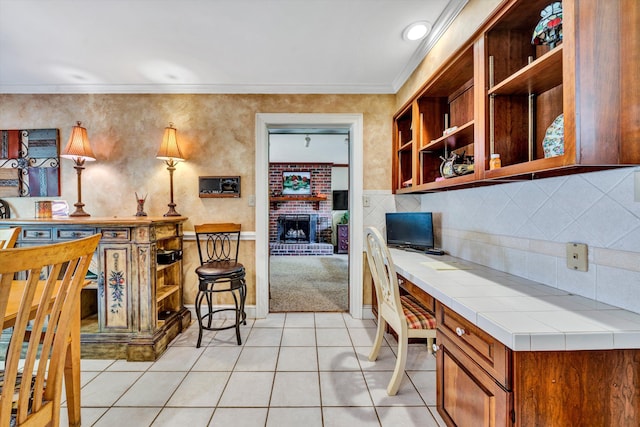 kitchen with tile counters, backsplash, ornamental molding, light colored carpet, and brick wall