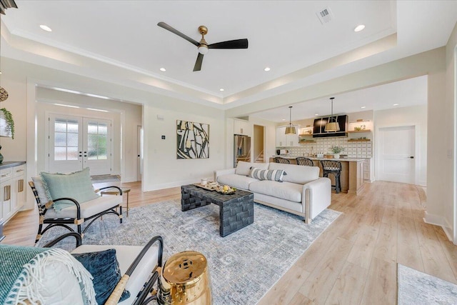 living area with baseboards, light wood-type flooring, recessed lighting, french doors, and a raised ceiling