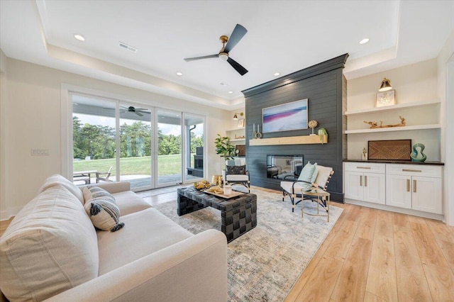 living room featuring built in features, visible vents, a fireplace, light wood-style floors, and a raised ceiling