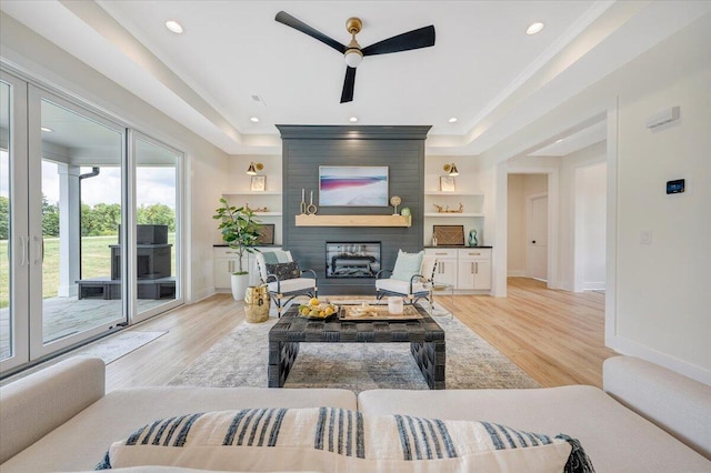 living area with a raised ceiling, a fireplace, and light wood-style floors