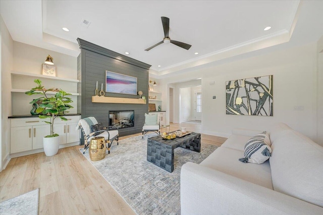 living area with light wood finished floors, built in shelves, a large fireplace, recessed lighting, and a raised ceiling