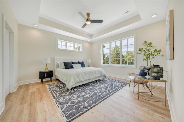 bedroom with ceiling fan, baseboards, light wood-type flooring, and a tray ceiling