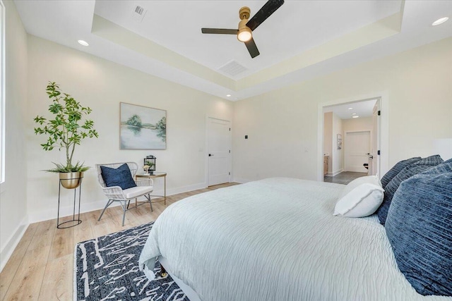 bedroom with visible vents, light wood-style flooring, a raised ceiling, and baseboards