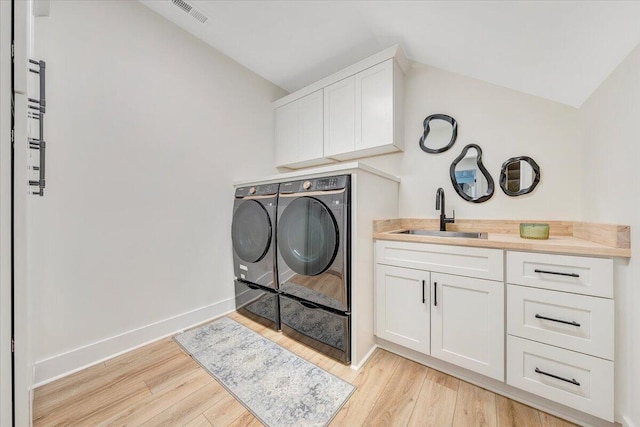 clothes washing area featuring visible vents, light wood finished floors, cabinet space, a sink, and independent washer and dryer