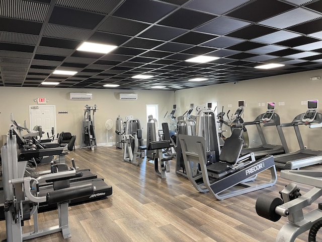 exercise room with a drop ceiling, wood finished floors, and a wall mounted air conditioner