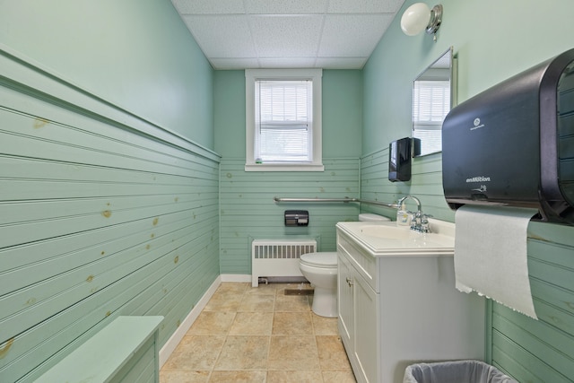 bathroom with a drop ceiling, vanity, wooden walls, toilet, and tile patterned flooring