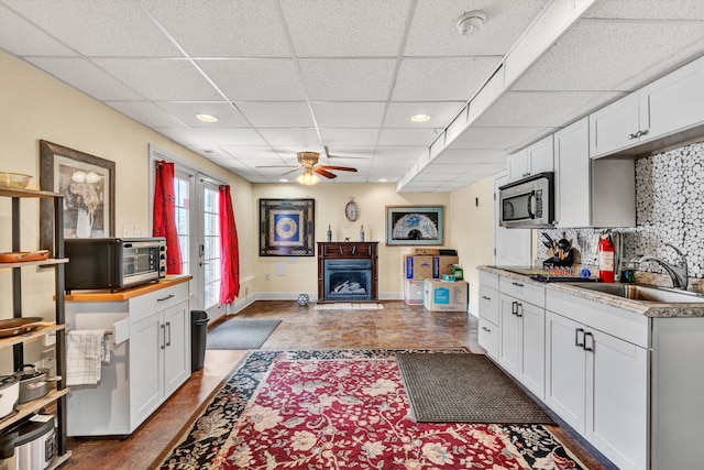 kitchen featuring white cabinetry, ceiling fan, sink, and backsplash