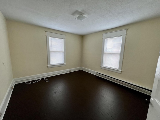 empty room featuring a textured ceiling, a baseboard heating unit, and hardwood / wood-style floors