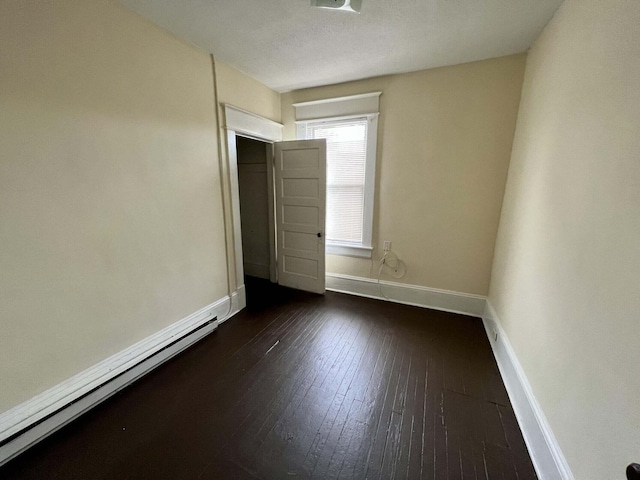 unfurnished room with dark wood-type flooring, a baseboard heating unit, and a textured ceiling