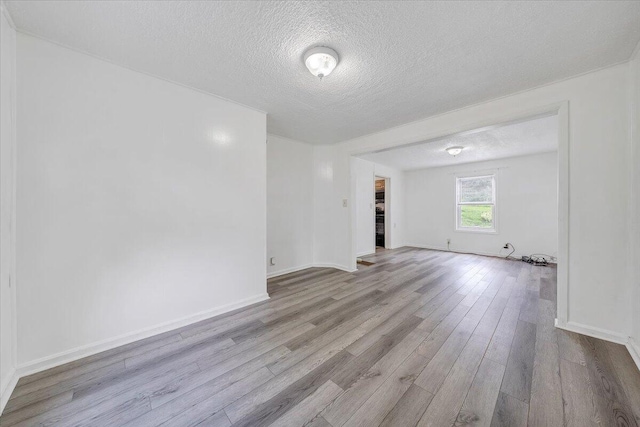 empty room with a textured ceiling, baseboards, and wood finished floors