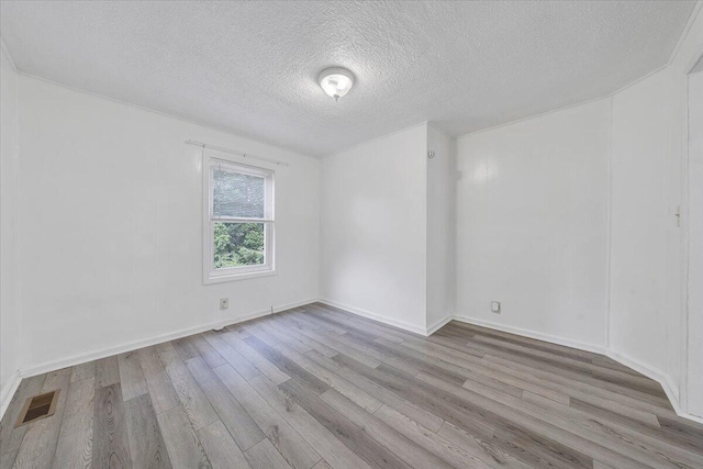 unfurnished room featuring a textured ceiling, wood finished floors, visible vents, and baseboards