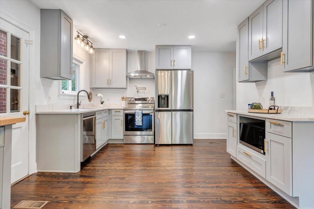 kitchen featuring appliances with stainless steel finishes, dark hardwood / wood-style floors, wall chimney range hood, and gray cabinetry