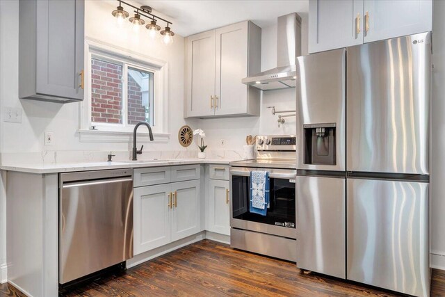 kitchen with stainless steel appliances, wall chimney exhaust hood, sink, light stone counters, and dark wood-type flooring