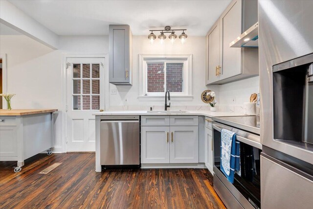 kitchen with stainless steel dishwasher, dark hardwood / wood-style flooring, gray cabinetry, sink, and stove