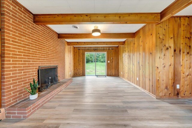 unfurnished living room featuring a fireplace, brick wall, hardwood / wood-style floors, and beamed ceiling