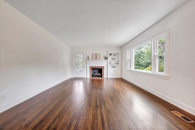 unfurnished living room with dark hardwood / wood-style flooring, built in shelves, and a brick fireplace