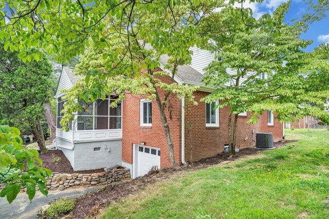 view of side of home featuring a lawn, a sunroom, a garage, and cooling unit