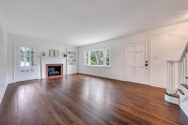 unfurnished living room with dark hardwood / wood-style floors, plenty of natural light, a brick fireplace, and built in shelves