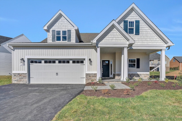 craftsman-style house with driveway, stone siding, and covered porch