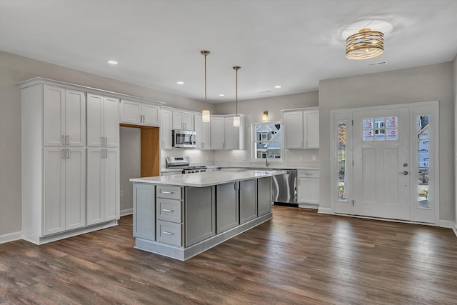 kitchen featuring appliances with stainless steel finishes, decorative light fixtures, white cabinets, a center island, and dark hardwood / wood-style floors