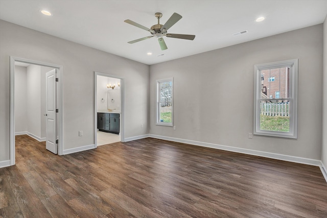 unfurnished bedroom with multiple windows, ensuite bathroom, ceiling fan, and dark hardwood / wood-style floors