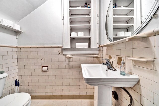 bathroom with toilet, tile patterned floors, and tile walls