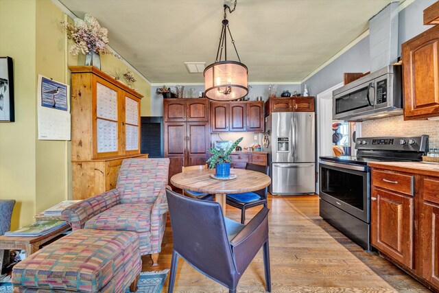 kitchen with backsplash, hanging light fixtures, appliances with stainless steel finishes, light hardwood / wood-style floors, and crown molding