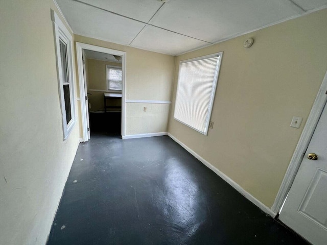 spare room featuring concrete floors, a drop ceiling, and a healthy amount of sunlight