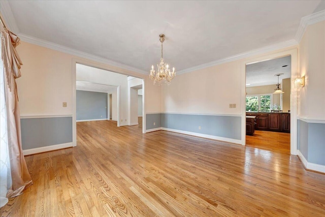 empty room featuring a notable chandelier, ornamental molding, and light hardwood / wood-style floors