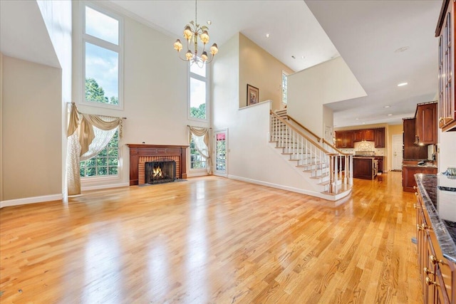 unfurnished living room with an inviting chandelier, a fireplace, light hardwood / wood-style floors, and a high ceiling