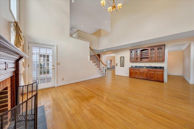 unfurnished living room with a high ceiling, a brick fireplace, an inviting chandelier, and light wood-type flooring