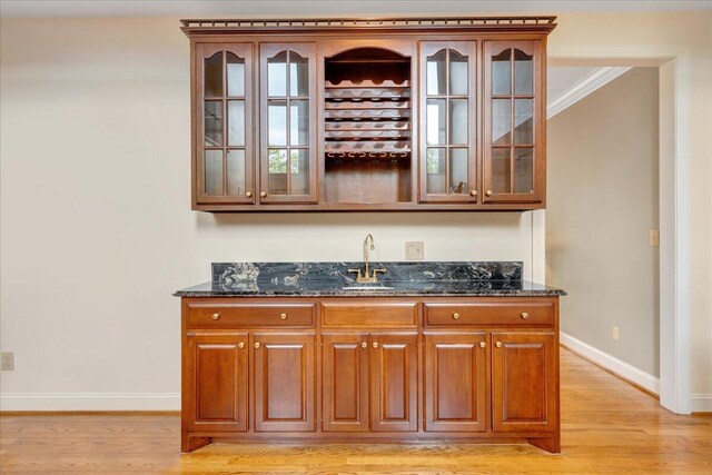 bar with crown molding, sink, light hardwood / wood-style floors, and dark stone countertops