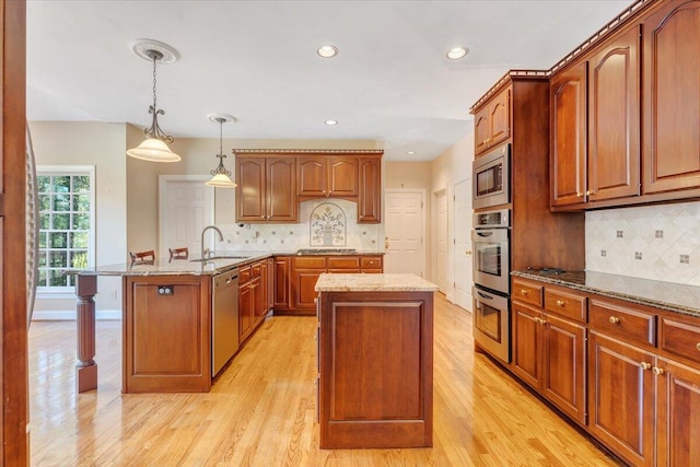 kitchen featuring pendant lighting, stainless steel appliances, light stone counters, a center island with sink, and light wood-type flooring