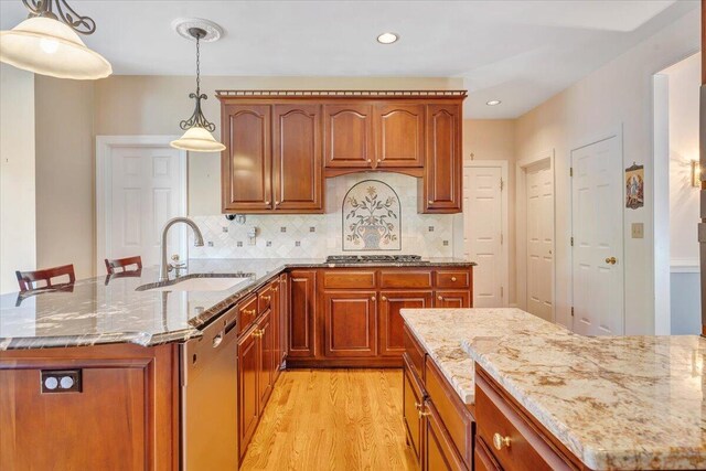 kitchen featuring sink, light stone counters, hanging light fixtures, light wood-type flooring, and appliances with stainless steel finishes