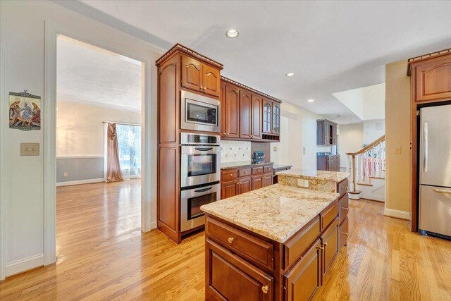 kitchen with stainless steel appliances, a center island, light stone counters, tasteful backsplash, and light hardwood / wood-style floors