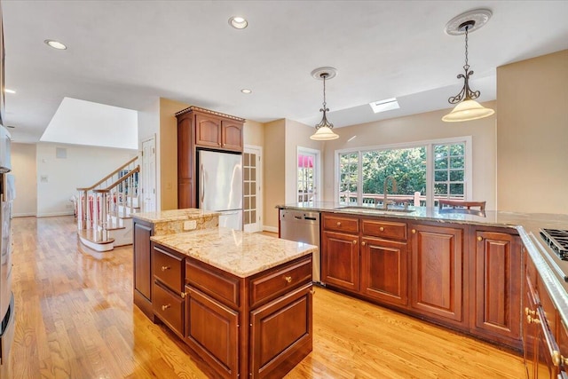 kitchen with sink, decorative light fixtures, light hardwood / wood-style flooring, appliances with stainless steel finishes, and a kitchen island