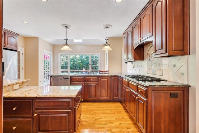 kitchen with sink, light stone counters, light wood-type flooring, appliances with stainless steel finishes, and pendant lighting