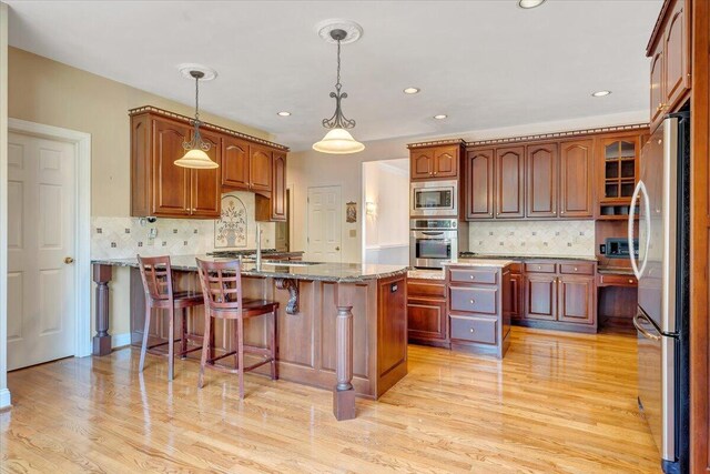 kitchen featuring light hardwood / wood-style flooring, appliances with stainless steel finishes, hanging light fixtures, light stone counters, and a kitchen island