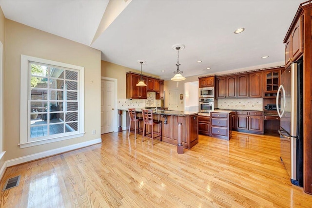 kitchen featuring a breakfast bar, appliances with stainless steel finishes, a kitchen island with sink, decorative light fixtures, and light wood-type flooring