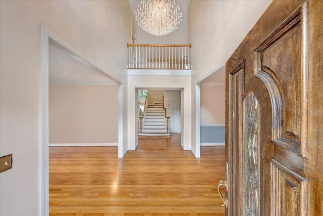 foyer with a high ceiling, ornamental molding, an inviting chandelier, and light wood-type flooring