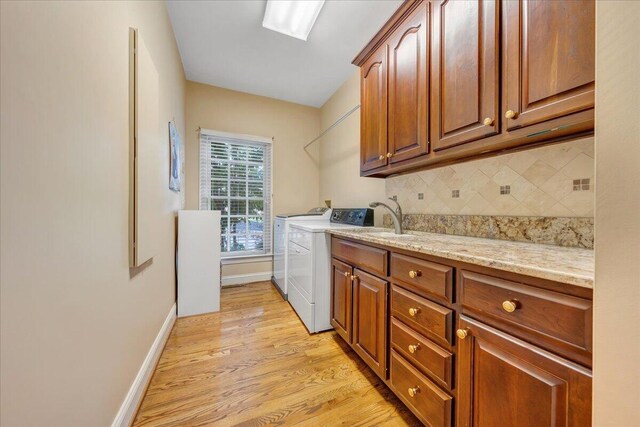 clothes washing area featuring cabinets, sink, washing machine and clothes dryer, and light hardwood / wood-style flooring