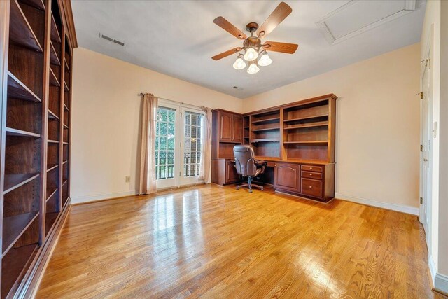 unfurnished office featuring ceiling fan, built in desk, and light hardwood / wood-style flooring