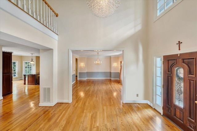 foyer entrance featuring a towering ceiling, a chandelier, and light hardwood / wood-style flooring